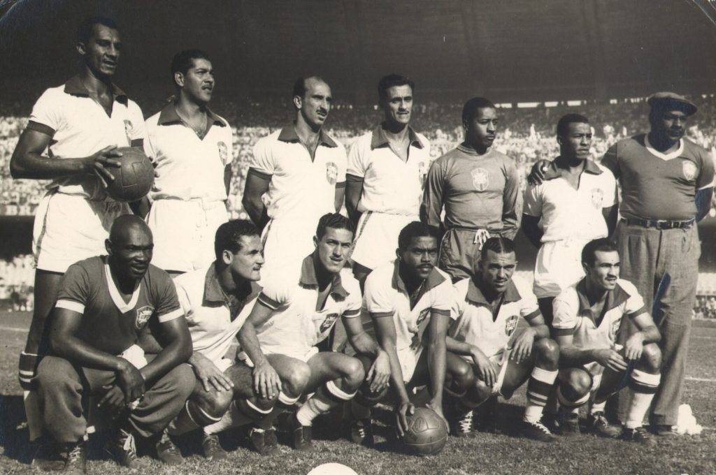 A group of 12 soccer members stands and kneels as photos of them are captured on the field before a match.